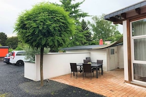 A patio with a table and chairs, a small tree, and a building with a window. - Holiday apartment with 1 bedroom (Siegburg)