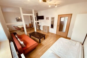 Habitació amb un sofà, un llit, una taula de fusta i un televisor fixat a la paret.