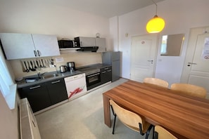 A compact kitchen with a microwave, oven, and sink. There is a wooden dining table with chairs. - Holiday apartment with 1 bedroom (Siegburg)