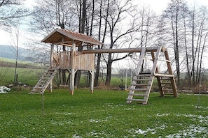 A wooden play structure with a slide and climbing ladders in a grassy field. - On the Freimuth Maria farm (Neukirchen b. Hl. Blut)