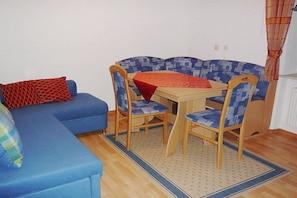 A small room with a blue sofa, a wooden dining table with two chairs, and a patterned rug. - On the Freimuth Maria farm (Neukirchen b. Hl. Blut)