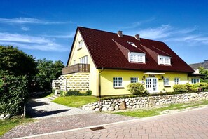 En gul bygning med rødt tag, en stenvæg og en belagt sti, der fører til indgangen.