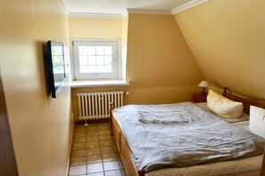 A bedroom with a bed, a window, a radiator, and a wall-mounted TV. - Friesenhaus Carl Jensen Holiday Apartment 3 (Wenningstedt-Braderup)