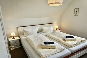 Ein Hotelzimmer mit zwei Betten, jeweils mit einem Kissen, einem Nachttisch mit einer Lampe und einer kleinen Schublade.