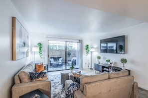 A modern living room with a sofa, coffee table, and a TV mounted on the wall. - 3-Bedroom Condo Near Reliant/NRG Stadium (Houston)