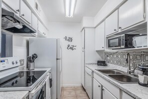 Une cuisine compacte avec des meubles blancs, un four à micro-ondes, un grille-pain et un réfrigérateur.