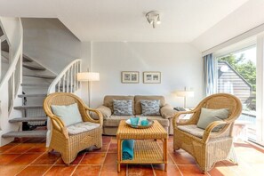 A living room with wicker furniture, a sofa, a coffee table, and a staircase. - House Cordula Holiday Apartment 38 (Wenningstedt-Braderup)