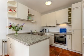 A kitchen with white cabinets, a granite countertop, a built-in oven, and a blue baking tray. - House Cordula Holiday Apartment 38 (Wenningstedt-Braderup)