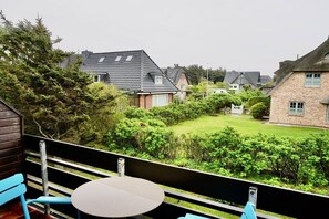 A balcony with a table and chairs, overlooking a well-maintained garden and neighboring houses. - House Cordula Holiday Apartment 38 (Wenningstedt-Braderup)