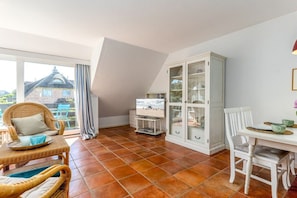 Ein Zimmer mit Esstisch, Stühlen, Fernseher und Schrank.