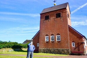 Eine Backsteinkirche mit einem Glockenturm, einem steinernen Sockel und blauem Himmel im Hintergrund.