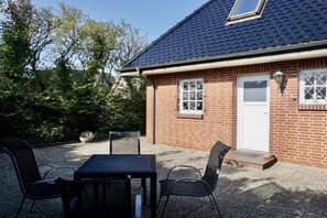 A brick house with a tiled roof, a white door, and a small porch with a table and chairs. - Bungalow with 2 bedrooms (Wenningstedt-Braderup)