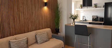 A modern kitchen with a wooden accent wall, a bar area, and a seating area with a sofa and chairs.
