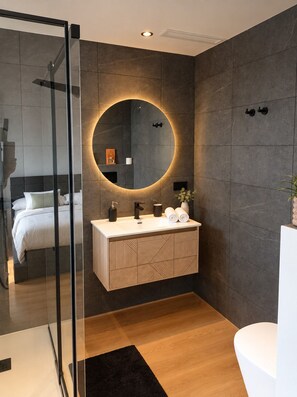Un bagno moderno con cabina doccia in vetro, uno specchio rotondo, un mobile bagno in legno e un water bianco.