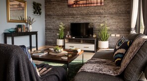 A modern living room with a flat-screen TV, a sofa, a coffee table with decorative items, and a bookshelf. - Tamnan Pool Resort Pattaya (Pattaya)