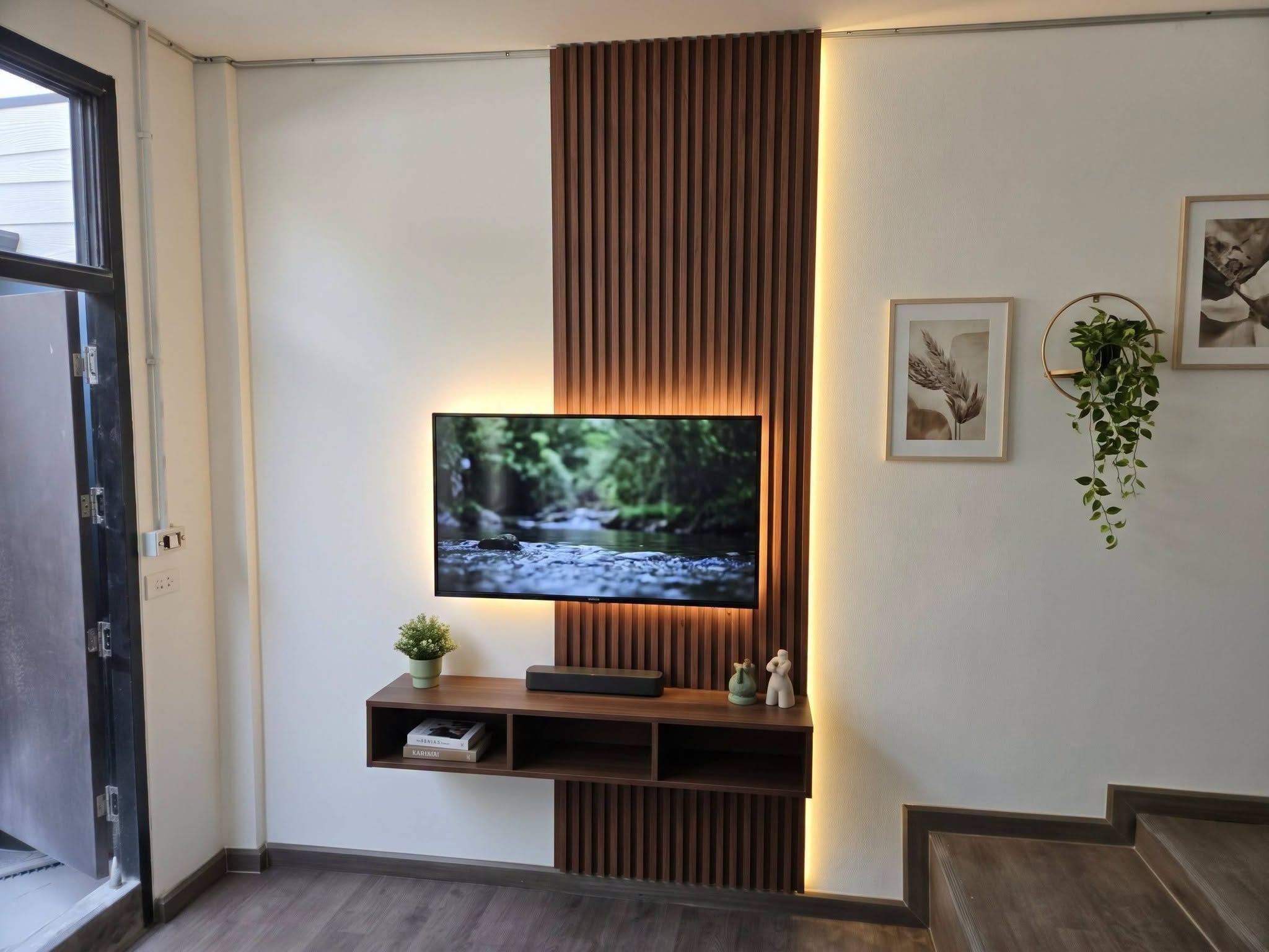 A flat-screen TV mounted on a wall with a wooden panel design, a small shelf with decorative items, and a framed picture to the right.