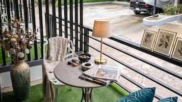 A balcony with a table, chairs, a lamp, and a vase with dried flowers.