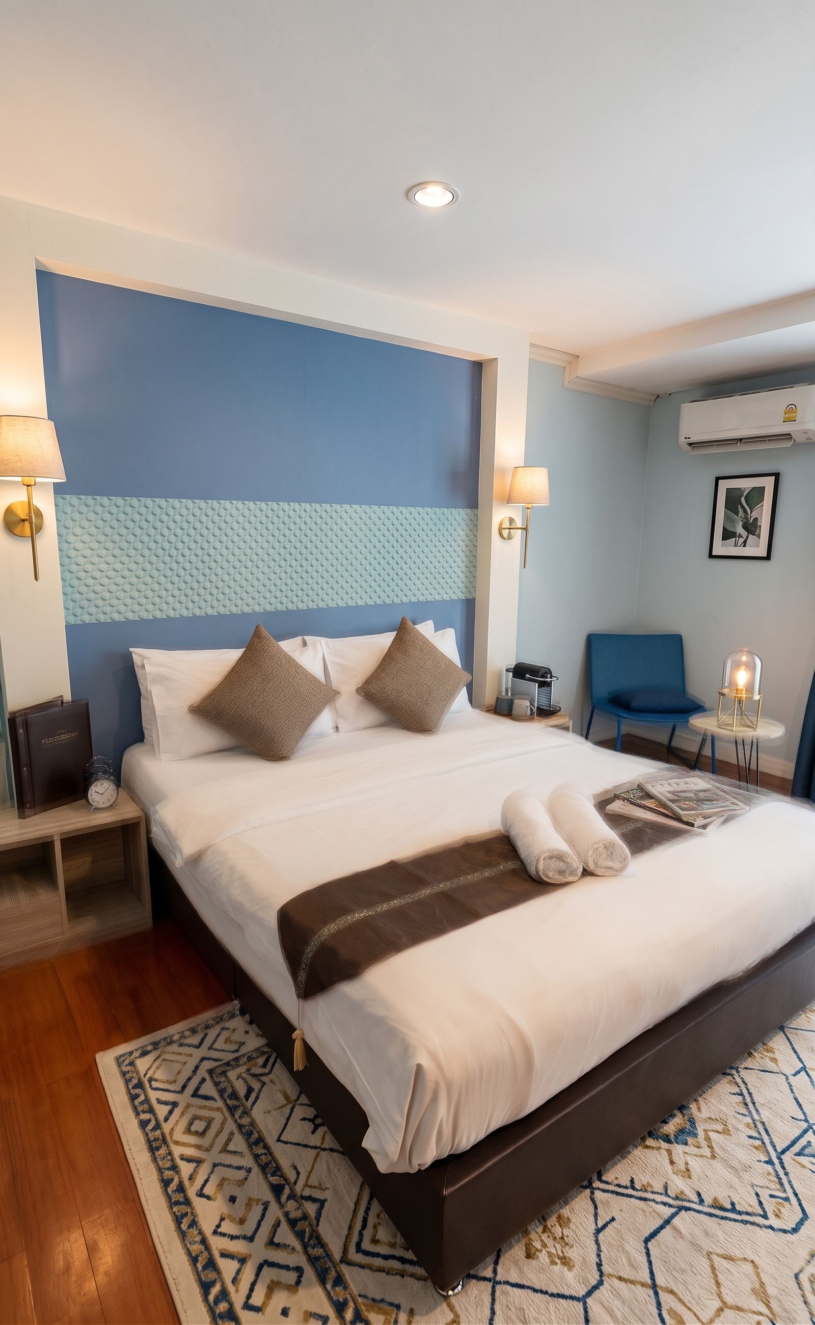 Een hotelkamer met een groot bed, twee bedlampen, een klok, een stoel, een bijzettafeltje en een airconditioning.