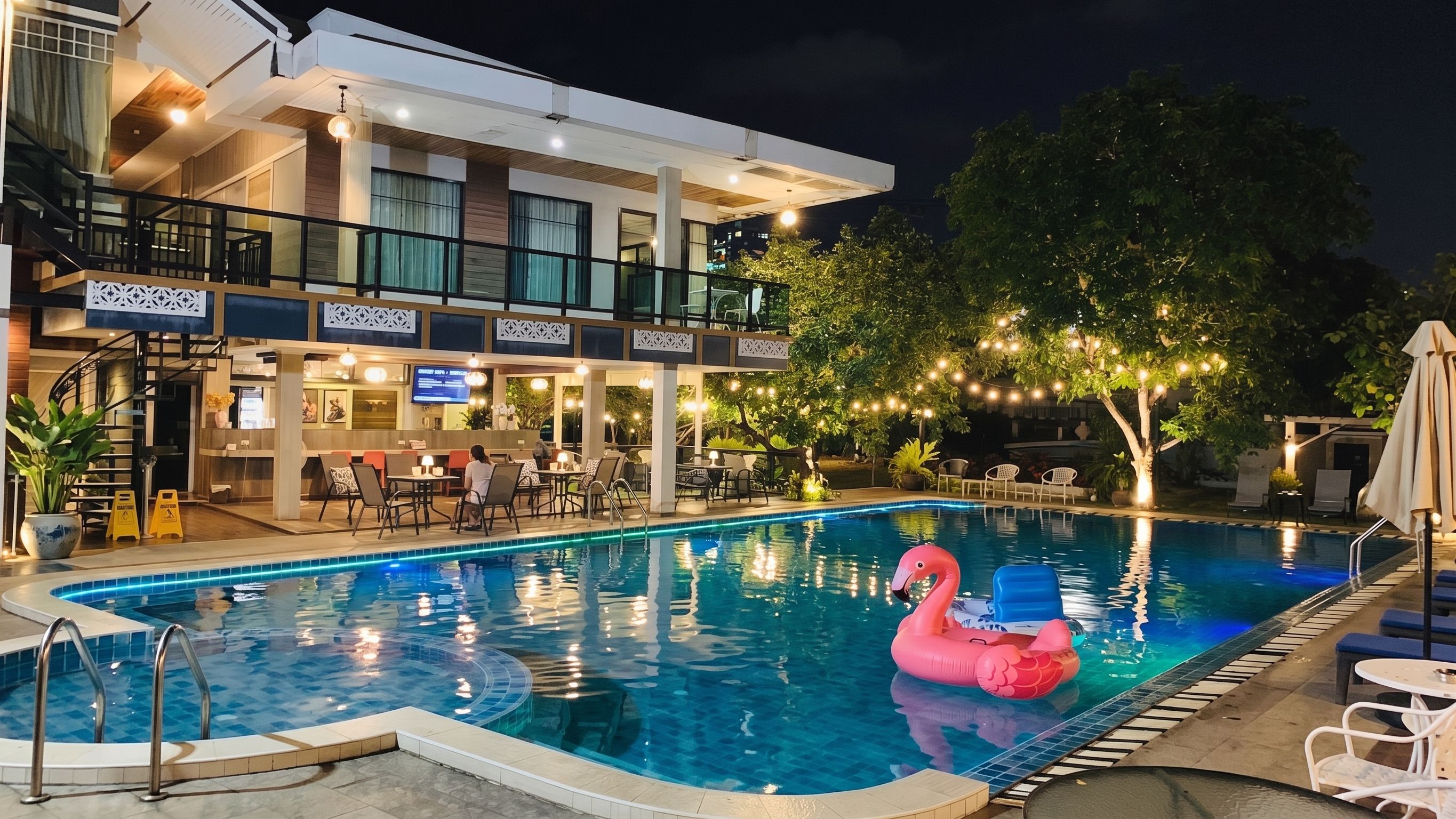 Une piscine agrémentée d’un flotteur en forme de flamant rose, entourée de chaises longues et d’un espace bar avec des sièges en plein air.
