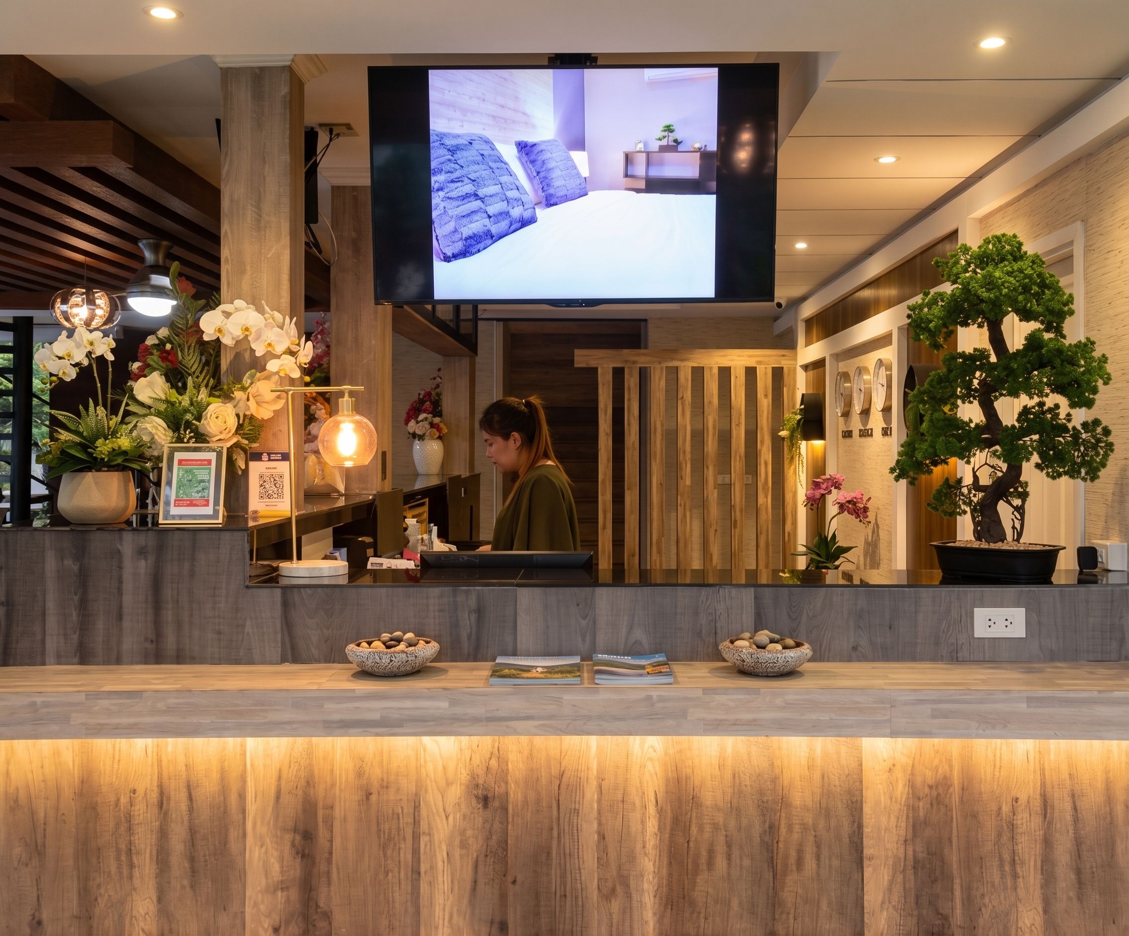 A reception desk with a flat-screen TV, wooden paneling, and potted plants.
