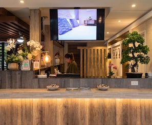 Un mostrador de recepción con un televisor de pantalla plana, paneles de madera y plantas en macetas.