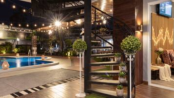 A modern indoor pool area with a wooden floor, a staircase, and decorative lighting.