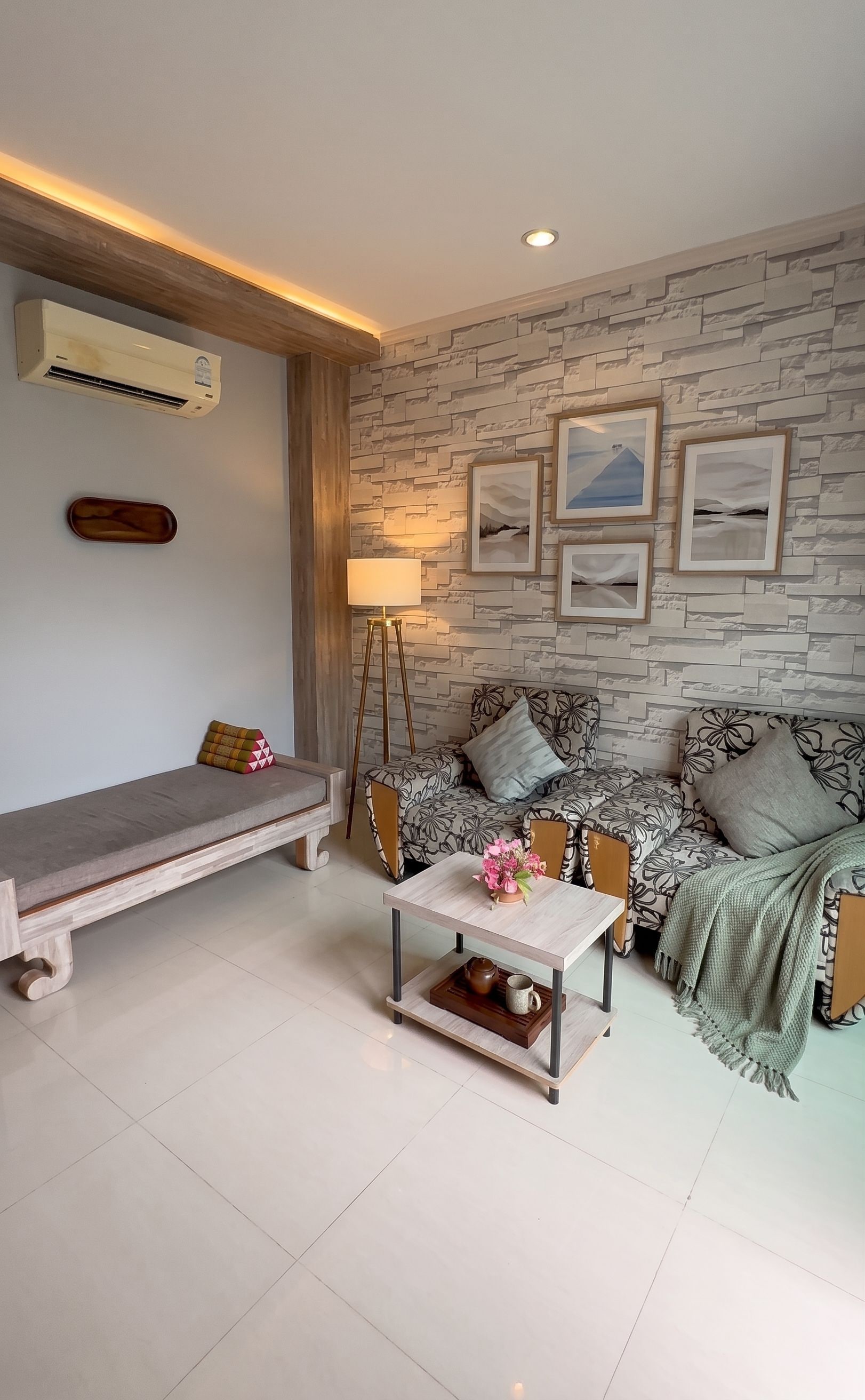 Una sala de estar moderna con pared de diseño que imita la piedra, un conjunto de sofás, una mesa de centro con objetos decorativos y una lámpara de pie.