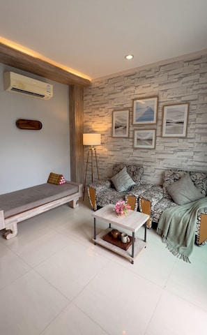 A modern living room with a stone-patterned wall, a sofa set, a coffee table with decorative items, and a standing lamp. - Tamnan Pool Resort Pattaya (Pattaya)