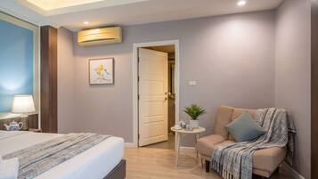 A hotel room with a bed, a chair, a small table with a plant, and a door leading to another room.