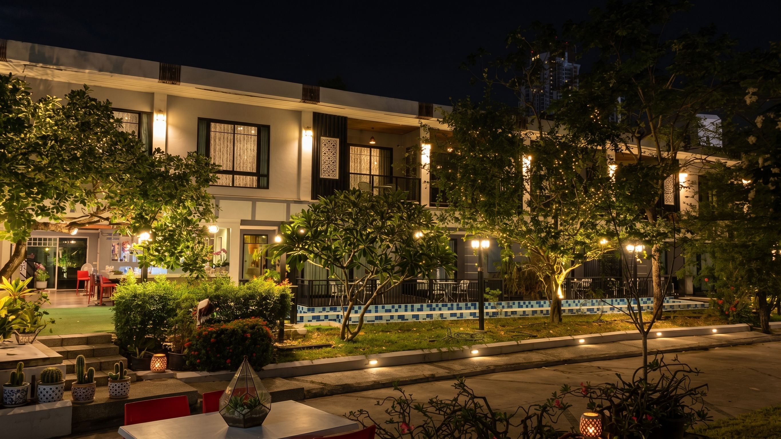 Un patio de hotel por la noche con mobiliario exterior, plantas en macetas e iluminación decorativa.