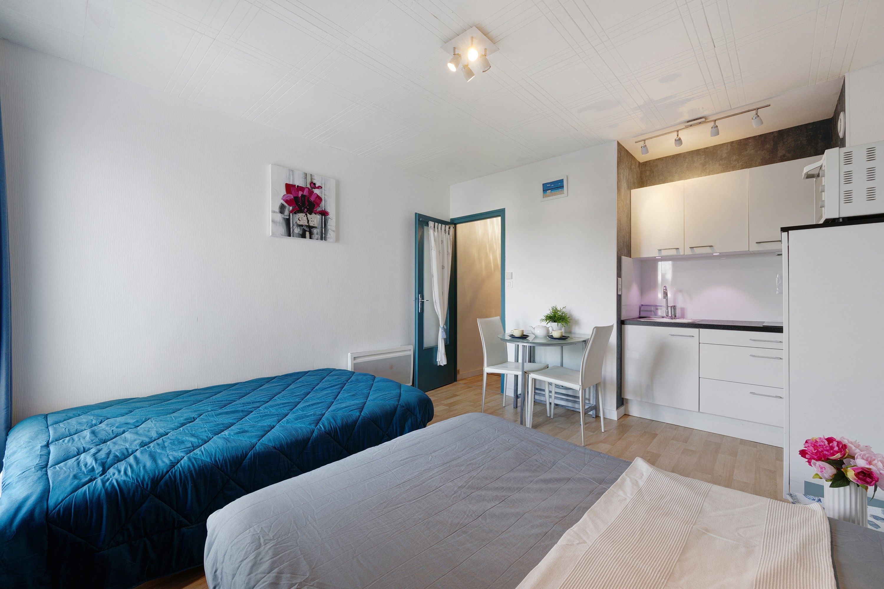 Ein kompaktes Hotelzimmer mit zwei Betten, einer Küchenzeile, einer kleinen Essecke und einem Badezimmer.