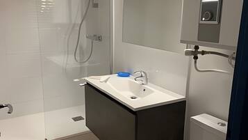 A modern bathroom with a glass shower enclosure, a white sink with a dark cabinet, and a white toilet.