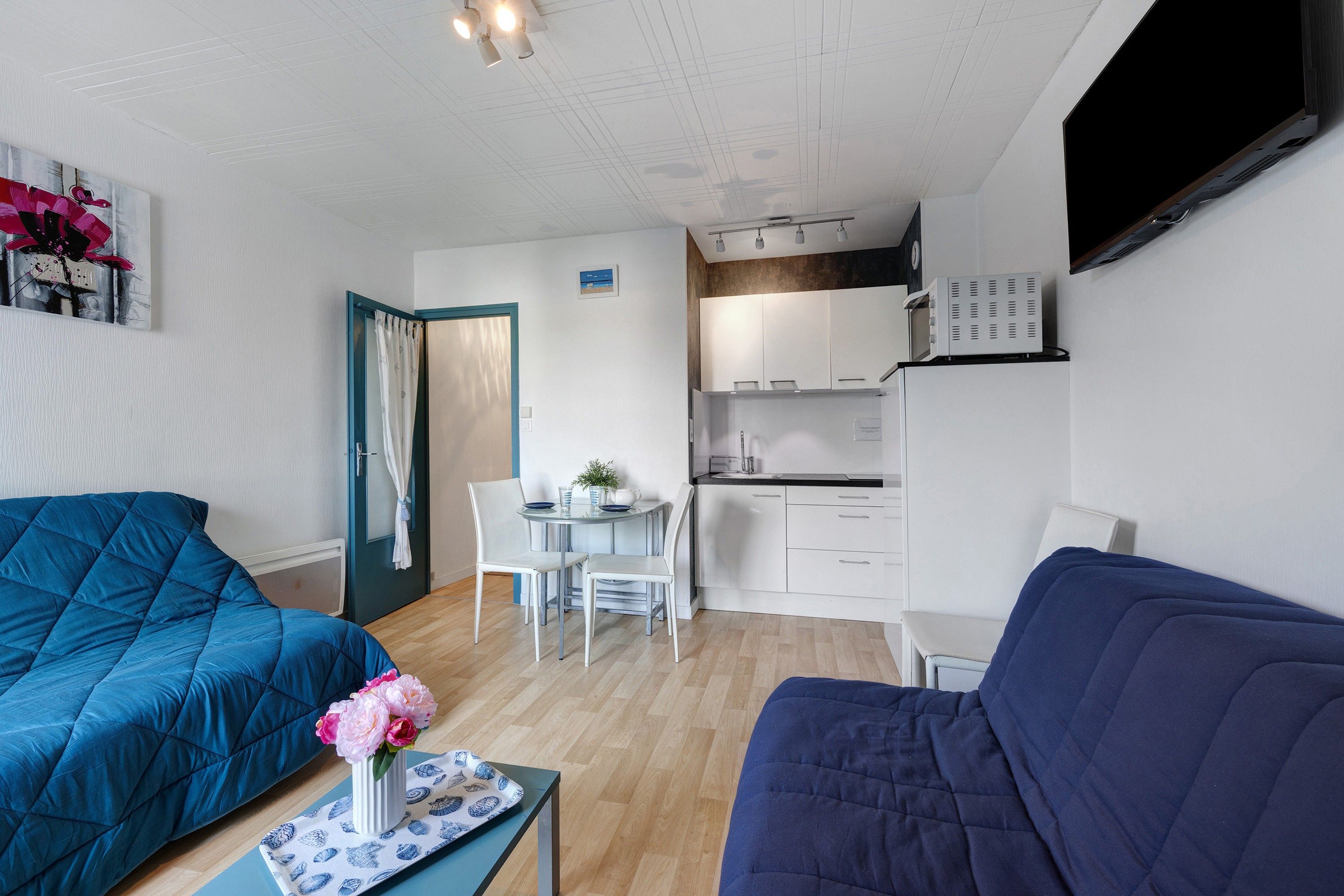 Ett kompakt bostadsutrymme med ett litet kök, en matplats och en sittgrupp med två soffor.