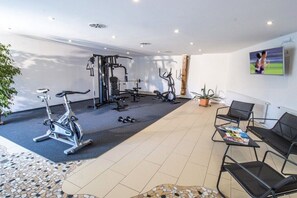 Une salle de sport équipée de matériel d’exercice, un espace détente avec des chaises et un téléviseur fixé au mur.