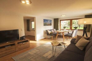 A living room with a television, sofa, coffee table, and a dining area with chairs and a table. - Holiday apartment with 1 bedroom (Oy-Mittelberg)