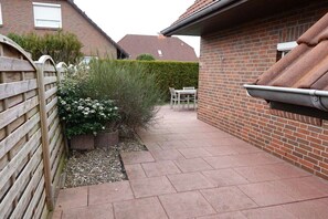 A residential backyard with a paved patio, a wooden fence, and a brick house. - Holiday home in Hooksiel with swimming pool (Hooksiel)