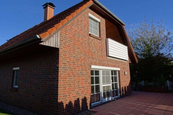 Une maison à deux étages, construite en briques, avec un toit à pignon, une cheminée et une porte-fenêtre coulissante.