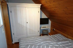 A bedroom with a bed, a wardrobe, a desk with a chair, and a television. - Holiday home in Hooksiel with swimming pool (Hooksiel)
