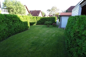 A well-maintained residential garden with a neatly trimmed lawn, a small tree, and a shed. - Holiday home in Hooksiel with swimming pool (Hooksiel)