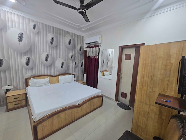 A hotel room with a bed, bedside tables, a wardrobe, a ceiling fan, an air conditioning unit, and a mirror.