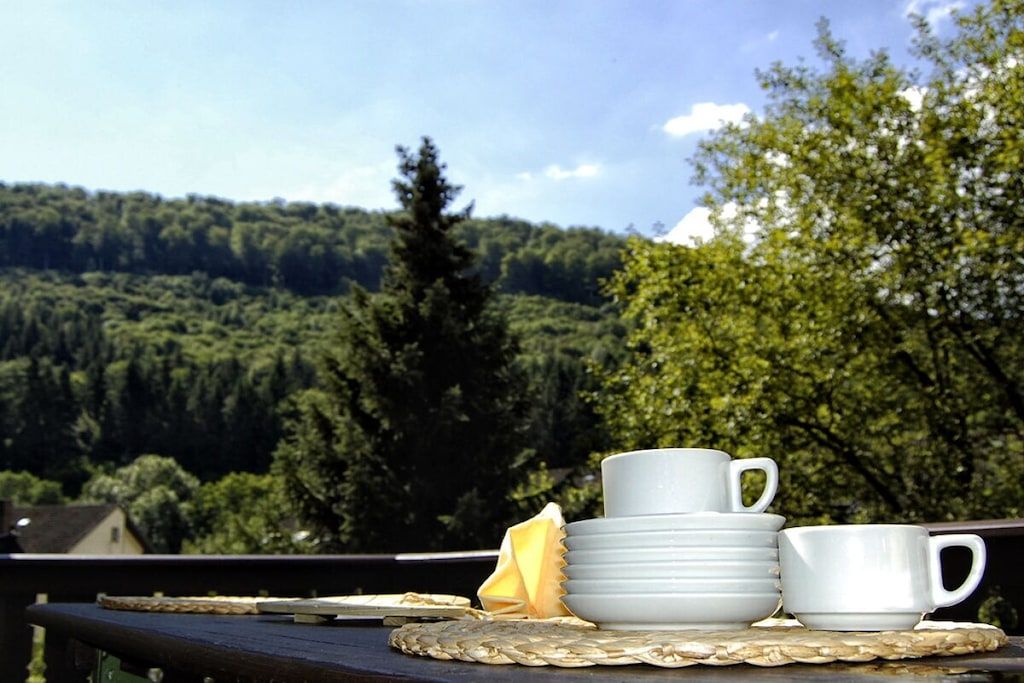 A table with stacked white cups and saucers, a folded napkin, and a woven placemat.