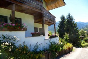 Ein traditionelles Chalet mit Balkon, umgeben von üppiger Vegetation und einer Bergkulisse.