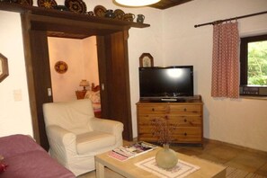 Ein Wohnzimmer mit einem Fernseher auf einer Holzkassette, einem weißen Sessel und einem Couchtisch mit einer Zeitschrift und einer Vase.