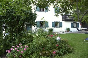 Ein weißes Gebäude mit grünen Fensterläden, umgeben von einem gepflegten Garten mit verschiedenen Pflanzen und Blumen.