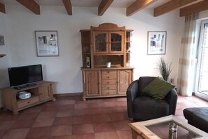 Een woonkamer met een houten kast, een televisie, een leren bank en een raam met gordijnen.