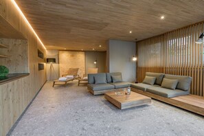 Ein modernes Wohnzimmer mit Holzboden, einem grauen Sofagarnitur, einem Couchtisch und einer Sitzecke mit Sessel und kleinem Tisch.