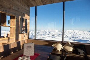 A room with a large window overlooking a snowy mountain landscape, a wooden wall, and a table with a sign reading 'TAFEL ZUNDER'. - Holiday apartment with 1 bedroom (Oberstdorf)