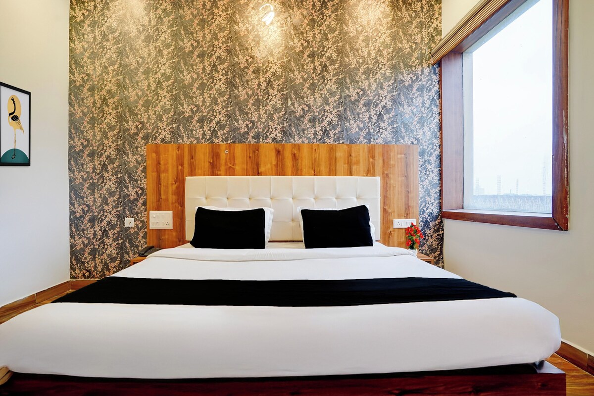 A hotel room with a large bed, wooden headboard, and a floral-patterned wall.
