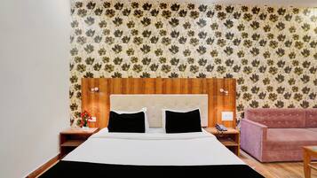 A hotel room with a bed, a wooden headboard, a pink sofa, and floral wallpaper.