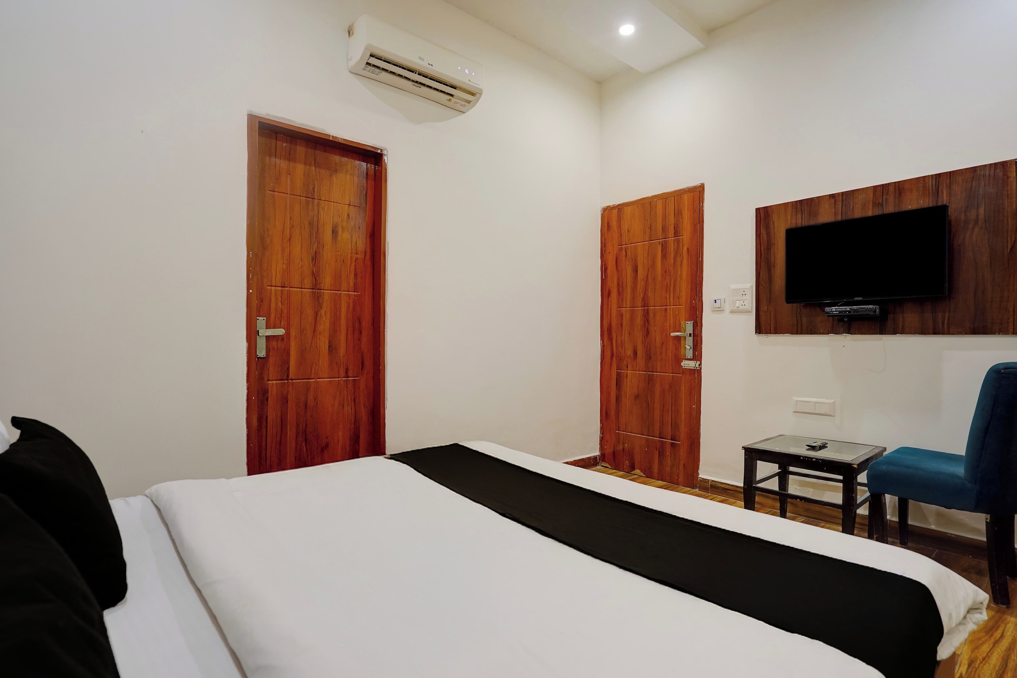 Habitación de hotel con una cama, un televisor montado en la pared y dos puertas de madera.